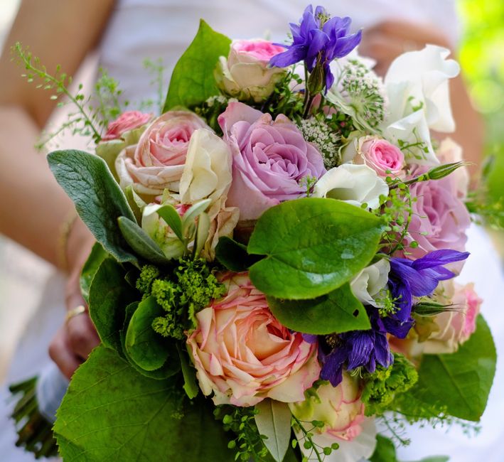 A bouquet of fresh floral arranged for a wedding gift features large pale pink and cream roses, complemented by deep purple flowers, possibly delphiniums, and accented with delicate white filler flowe